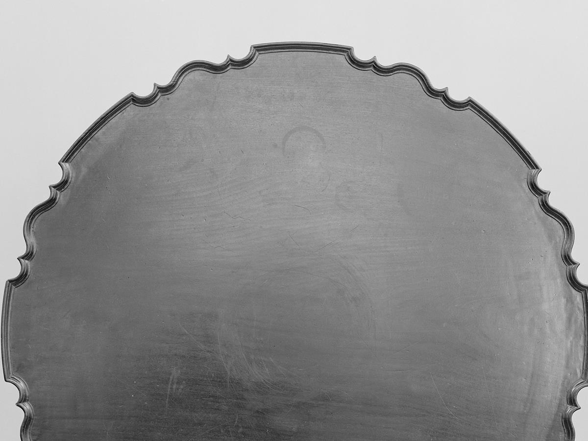 Close-up of the scalloped hand-carved pie-crust molded edge of an antique 18th-century mahogany tilt-top tea table